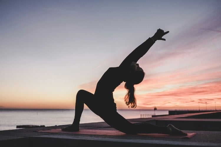 Woman does yoga on a pier at sunrise or sunset.